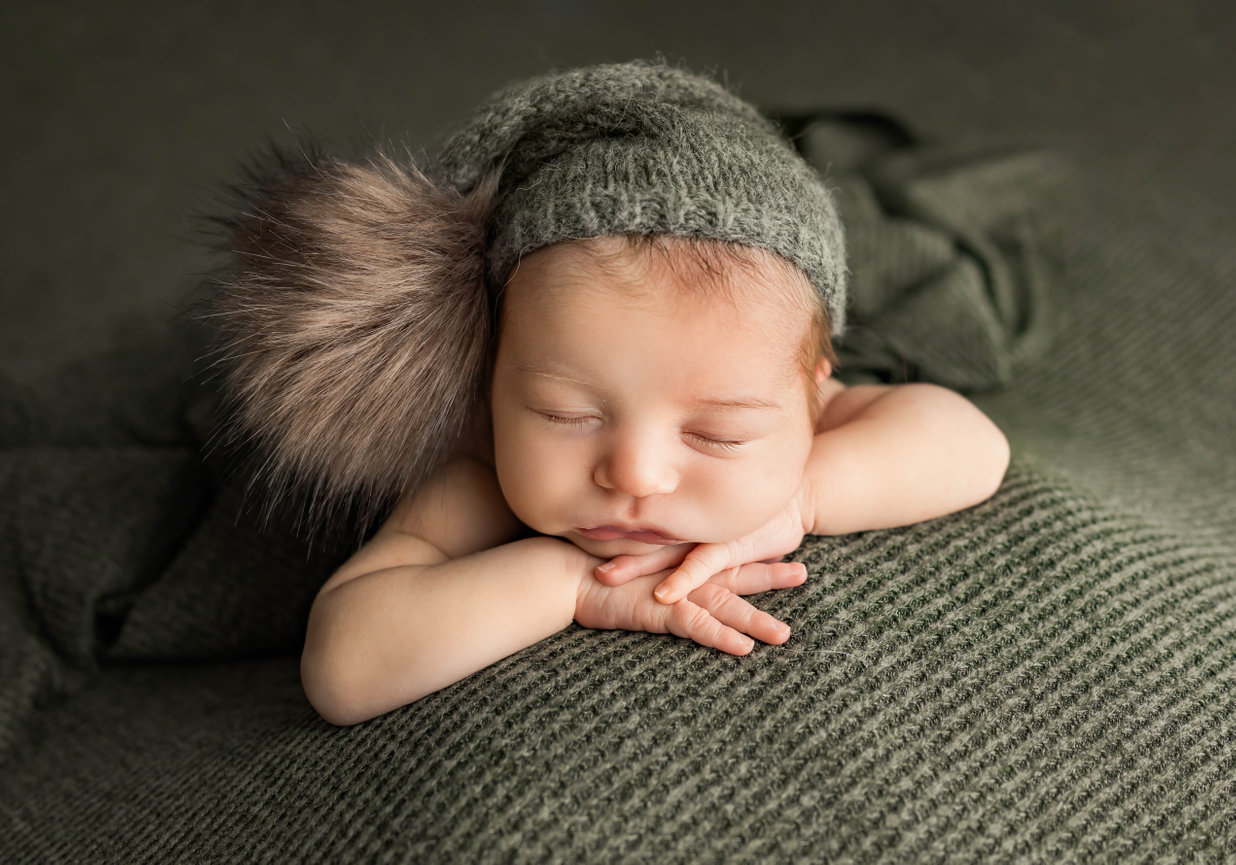Newborn wearing knit hat resting hands under chin