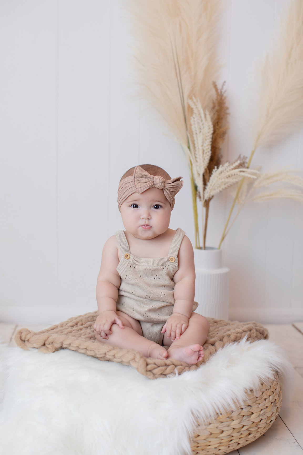 Baby in a pink romper sitting on a woven cushion