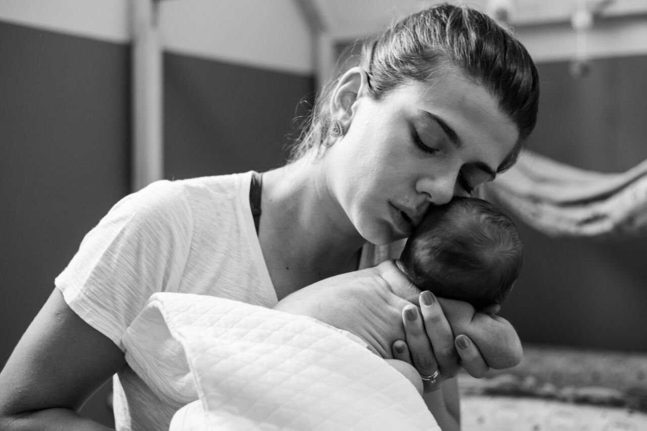 Mother kissing her newborn in a black and white portrait