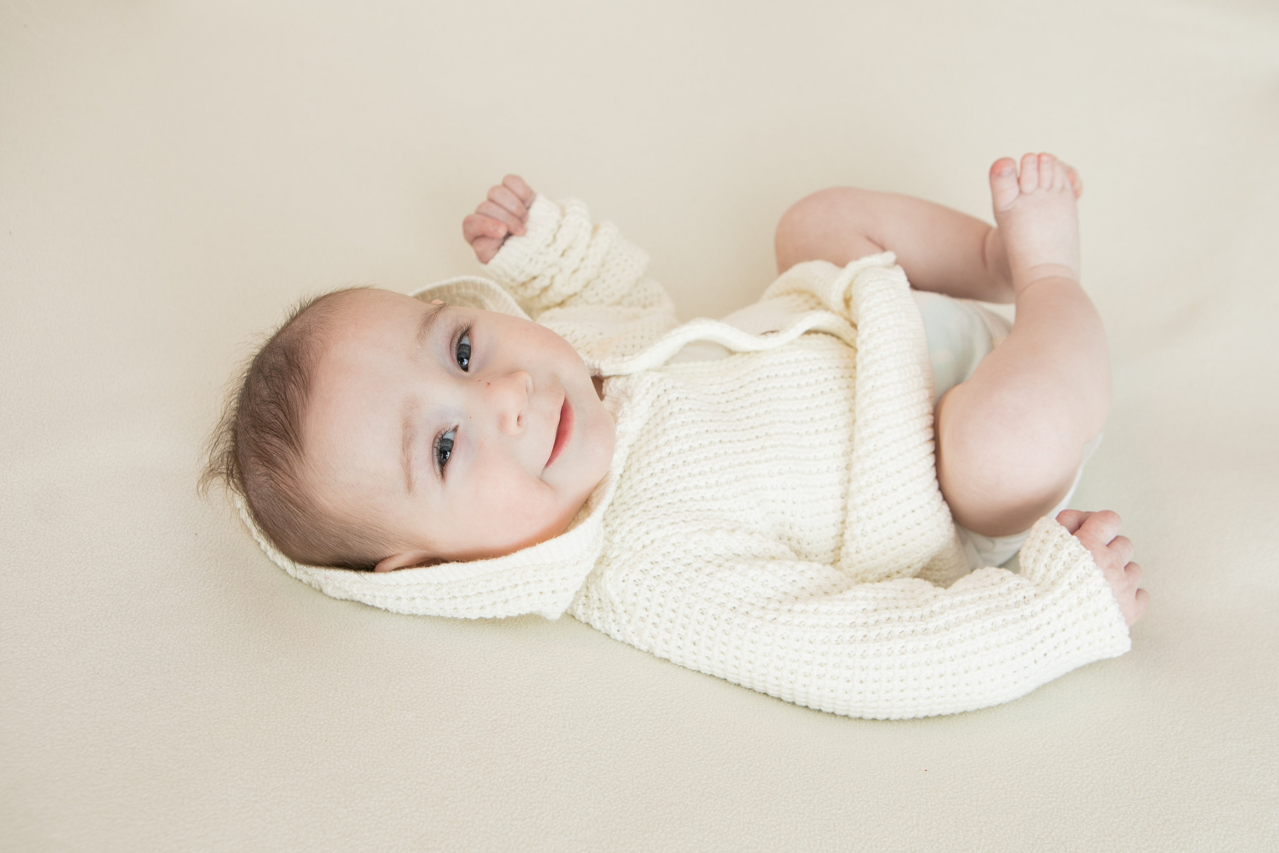 Baby holding their feet while lying on a beige backdrop
