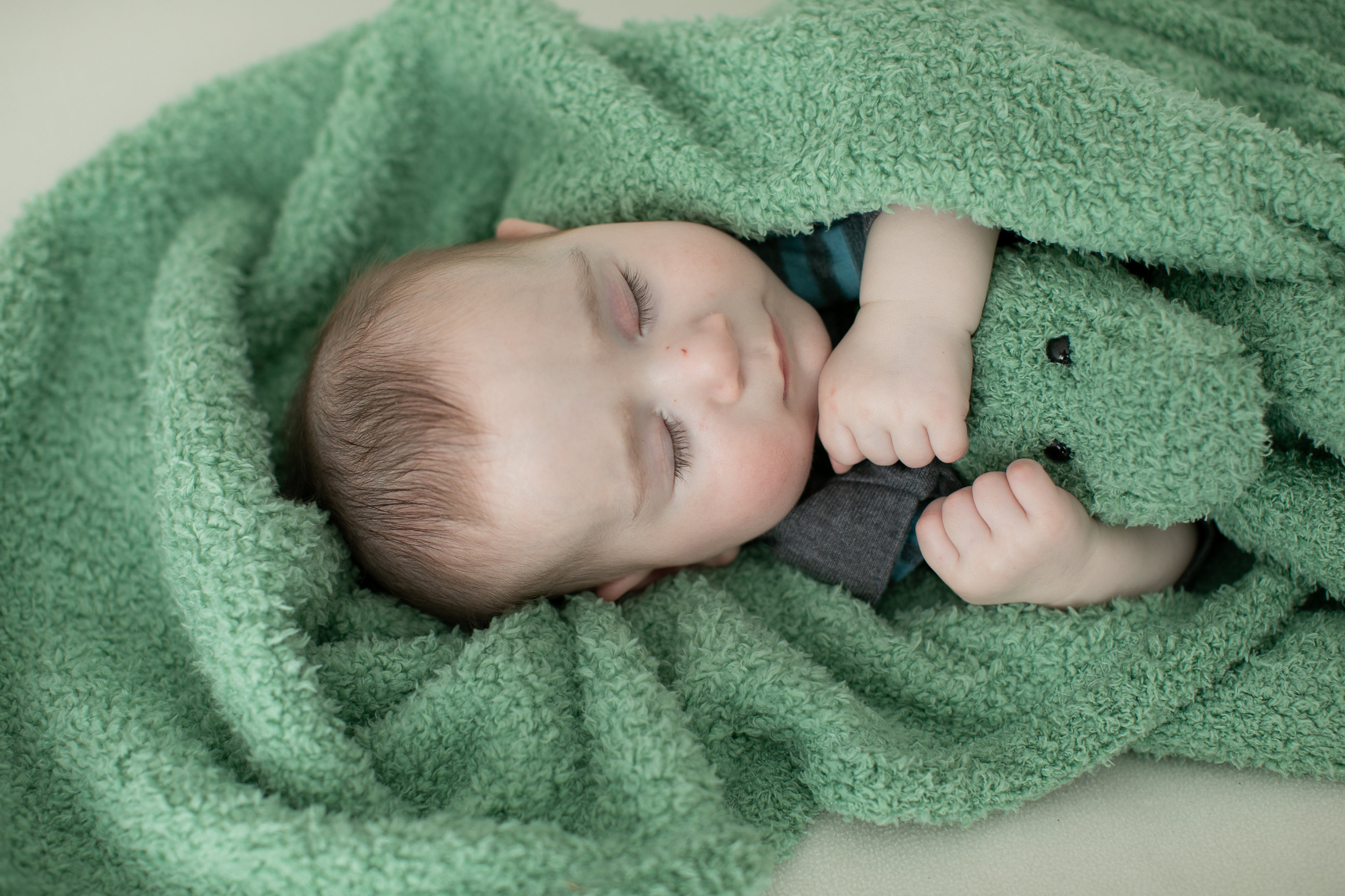 Baby resting on a green knitted blanket with a matching toy