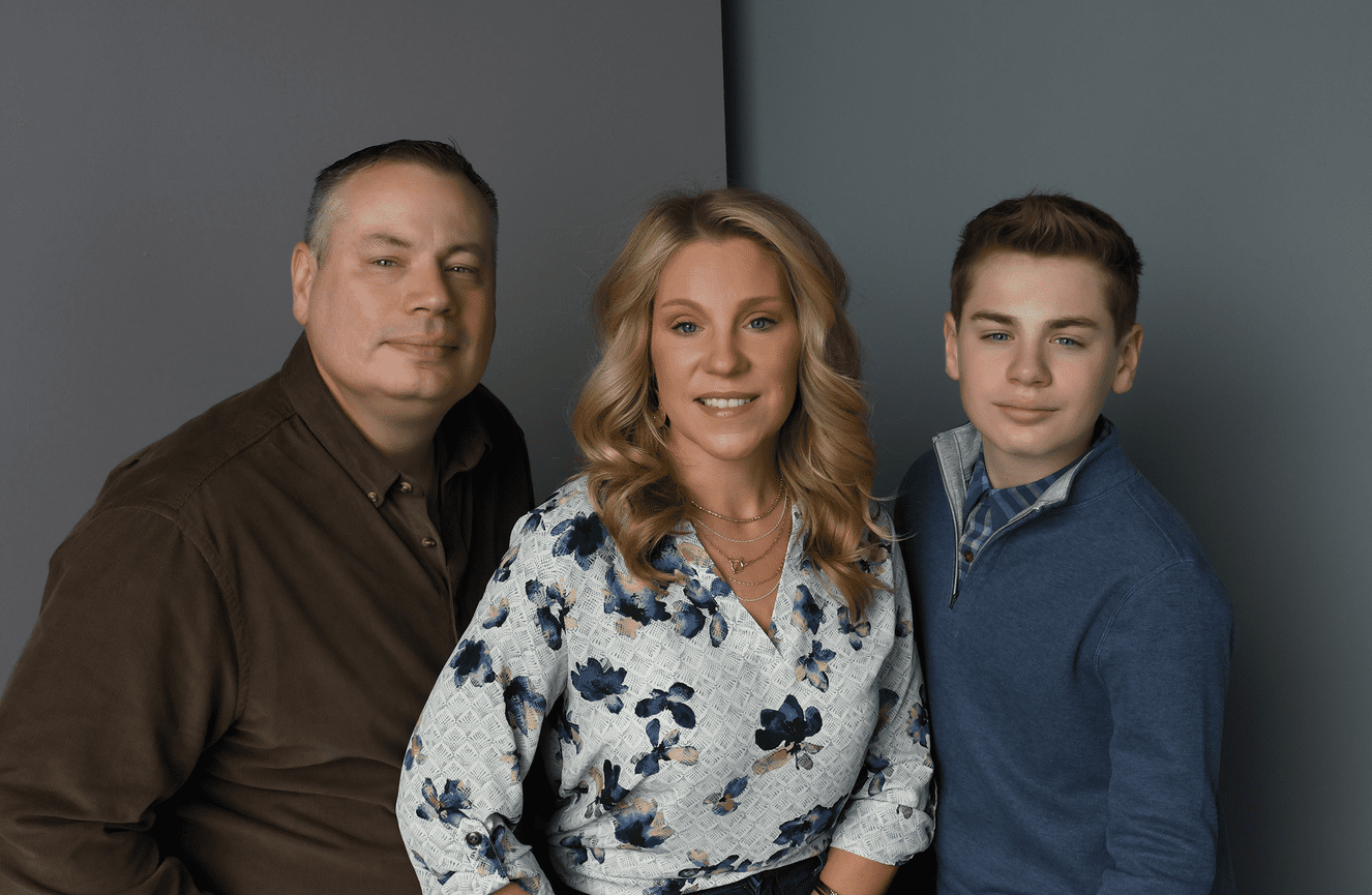 A mother in a floral blouse flanked by her husband and son for a family photo session.