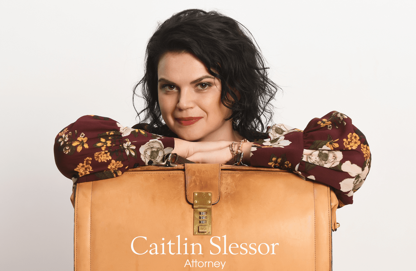 A self-assured female attorney with her arms folded across her tan leather briefcase.