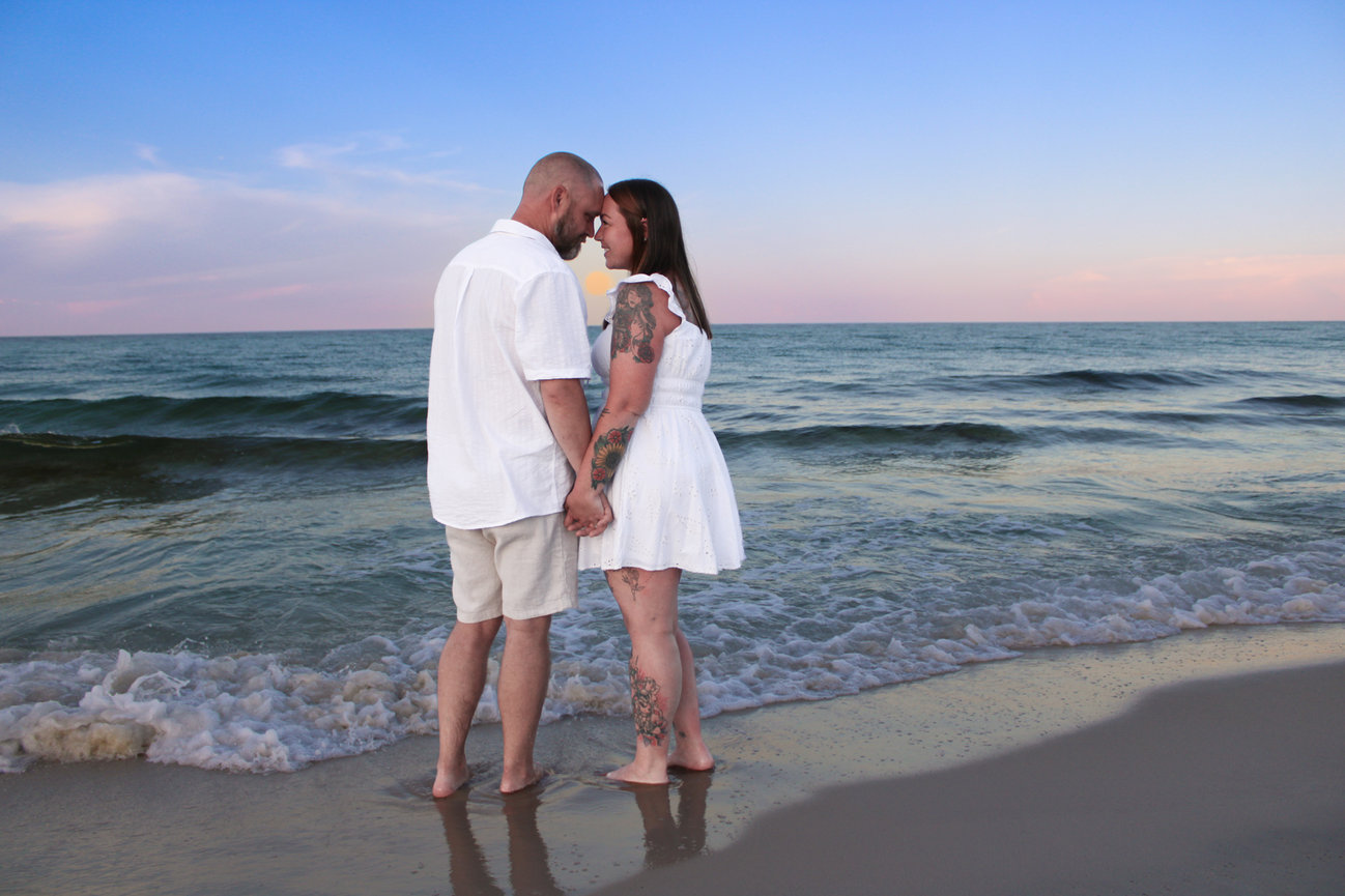 A couple embracing on the beach with waves behind them