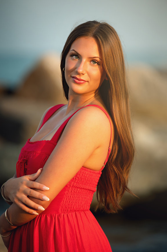 High School senior girl in a red dress poses outdoors with rocks in the background for her senior pictures along Lake Michigan