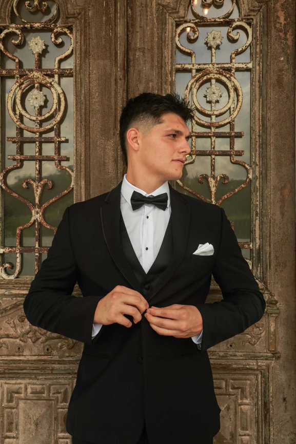 Groom adjusting his tuxedo in front of ornate carved doors.