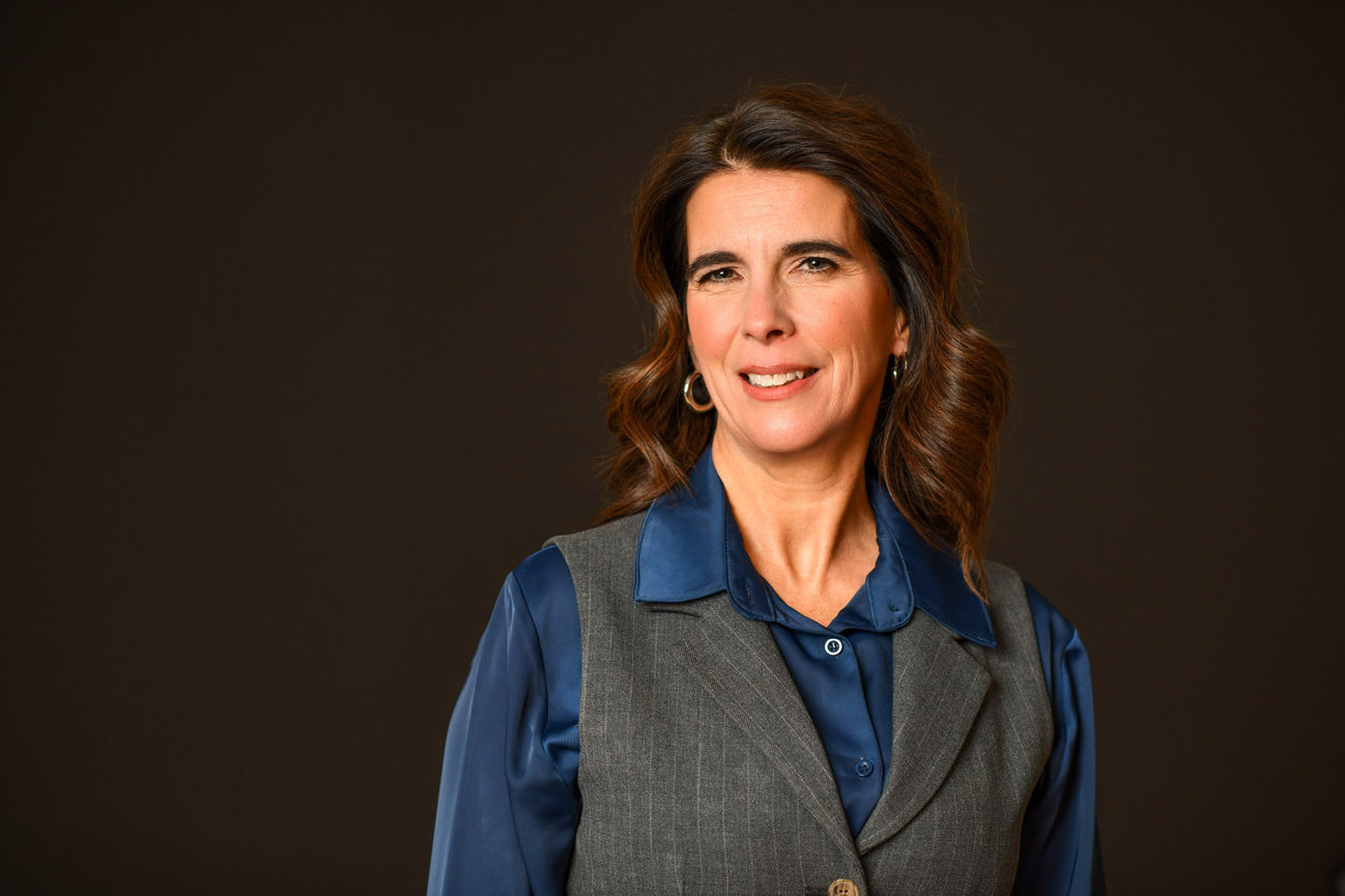 Woman with brown hair wearing a blue shirt and gray vest, smiling against a dark background for her branding and headshot session in Columbus Ohio