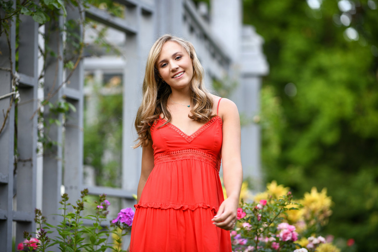 teenage girl in a red dress walking in a flower garden for senior pictures in Dublin OH.