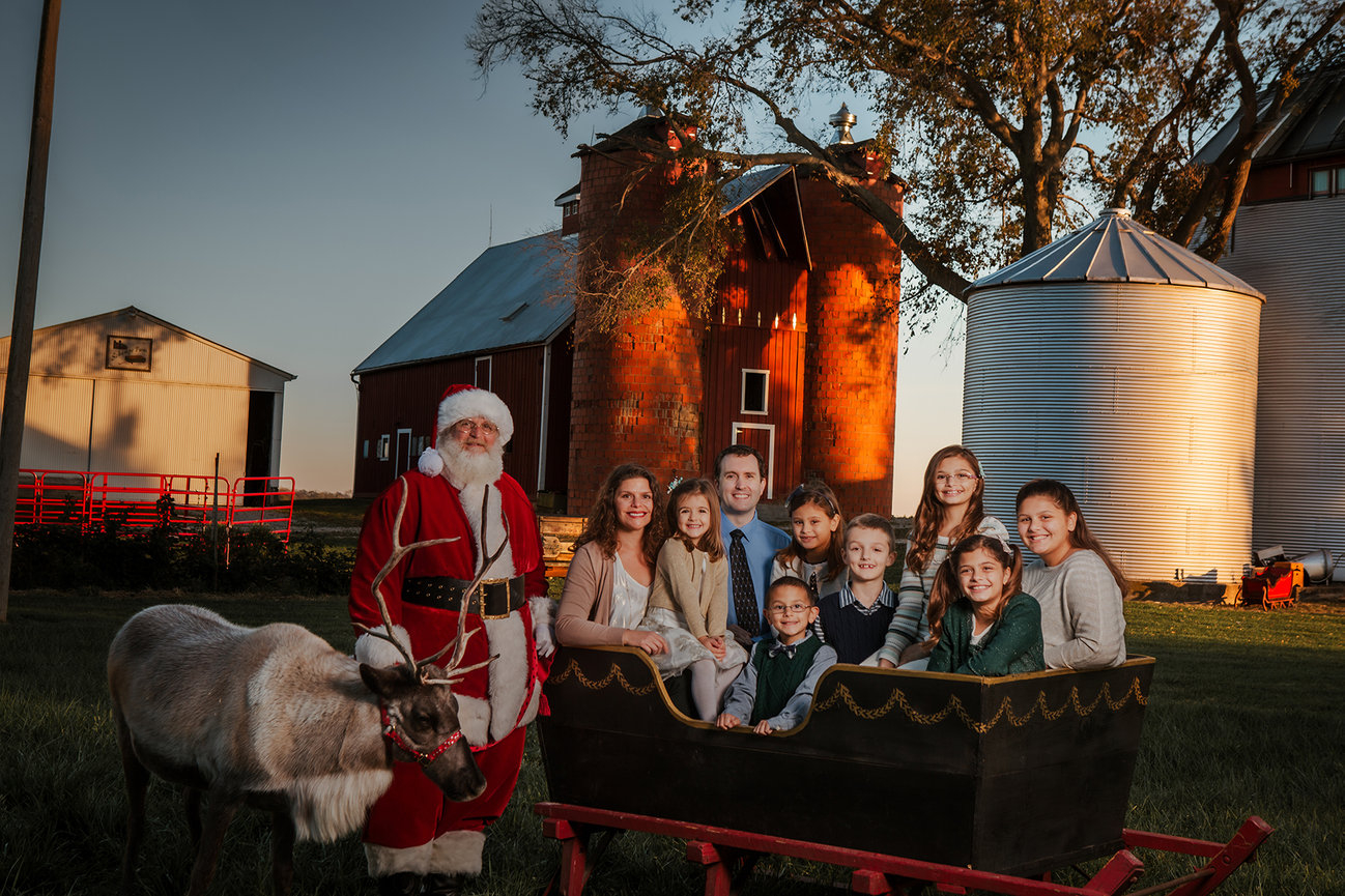 Family gathered with Santa and reindeer beside a sleigh at a previous holiday experience